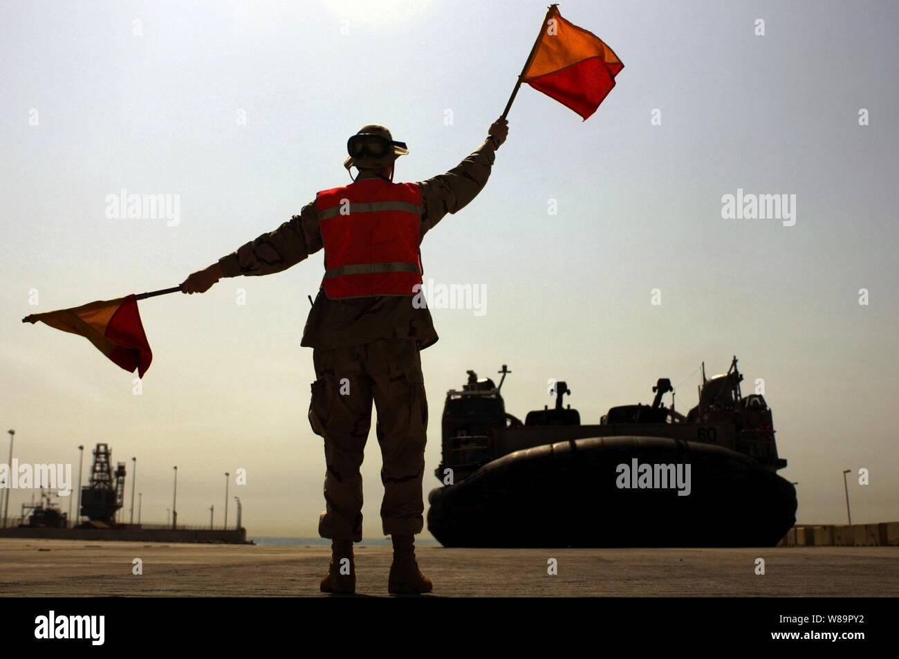 Navy Seaman Charles Shafer, from Beach Master Unit 2, uses flags to signal to the craftmaster of a Navy Landing Craft Air Cushion, or LCAC, at a Kuwaiti Naval Base staging area on June 1, 2005.  The LCAC, assigned to Assault Craft Unit 4 based in Little Creek, Va., is deployed in the Northern Persian Gulf with the USS Kearsarge (LHD 3) and USS Ashland (LSD 48) in support of transport operations with the 26th Marine Expeditionary Unit. Stock Photo