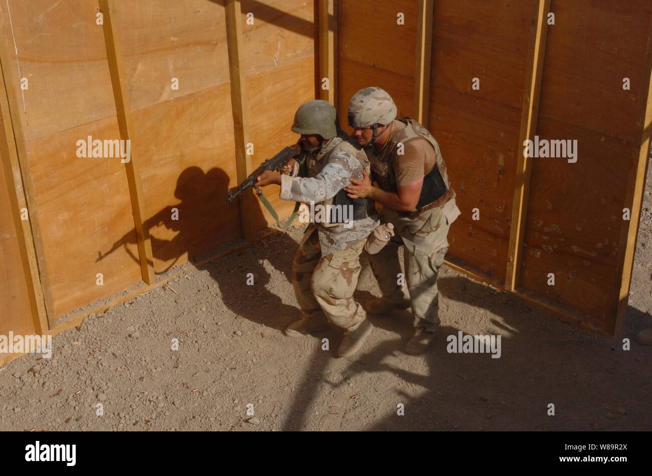 A U.S. Army soldier guides an 8th Division Iraqi Army soldier as he participates in a Shoot House live fire weapons training exercise at the Iraqi Army Compound on  Forward Operating Base Iskandariyah, Iraq, on July 30, 2005.  Members of the U.S. Army Multinational Training Team, part of the 155th Brigade Combat Team, are training Iraqi Army soldiers to increase their proficiency. Stock Photo