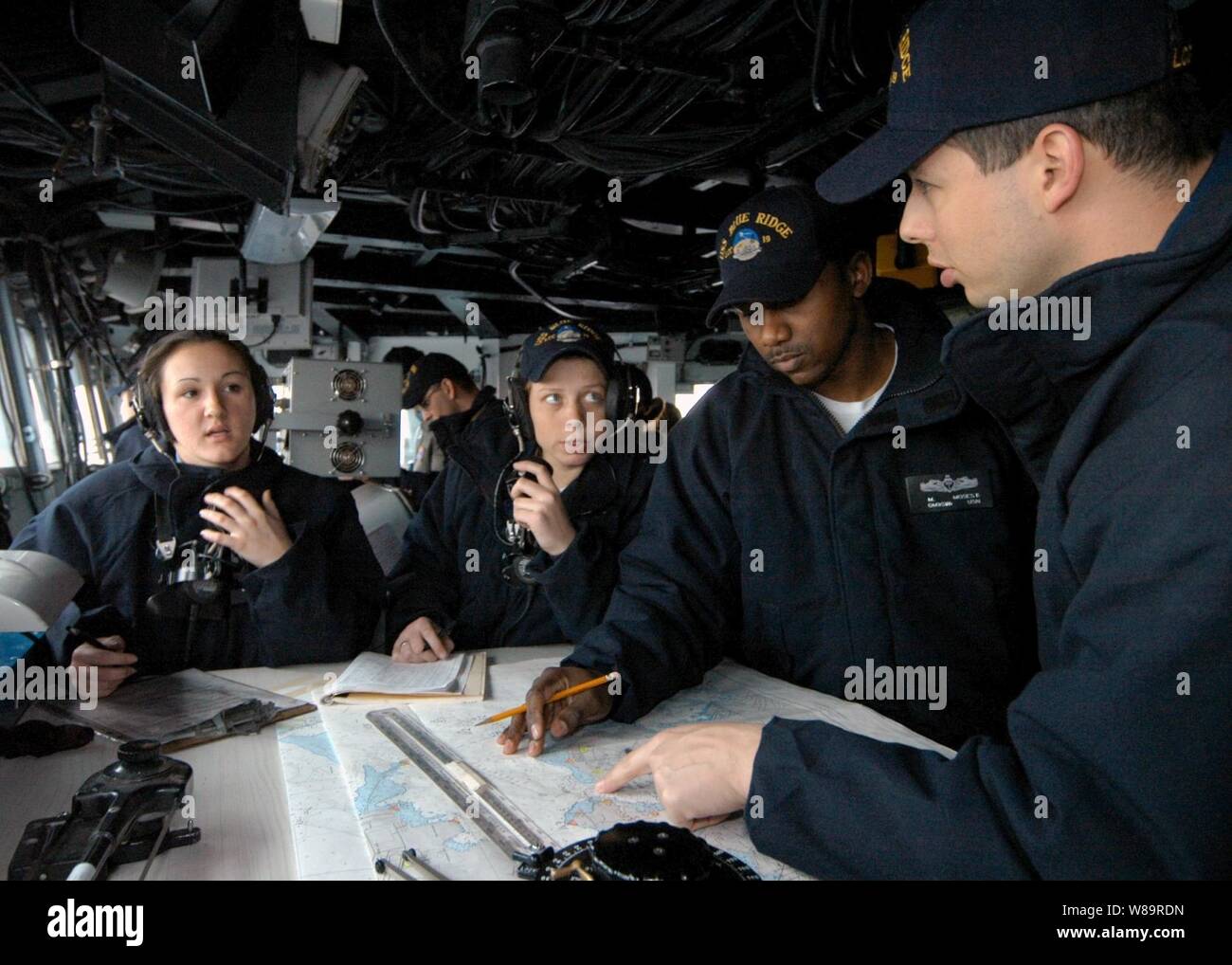 Phone talkers, the quartermaster and the ship's navigator gather around the chart table on the bridge of the USS Blue Ridge (LCC 19) as the ship sets the sea and anchor detail on Jan. 18, 2006.  These sailors, who are members of the Blue Ridge's sea and anchor navigation team, plot the ship's position and course as it gets underway for sea.  Blue Ridge is the Seventh Fleet command ship. Stock Photo
