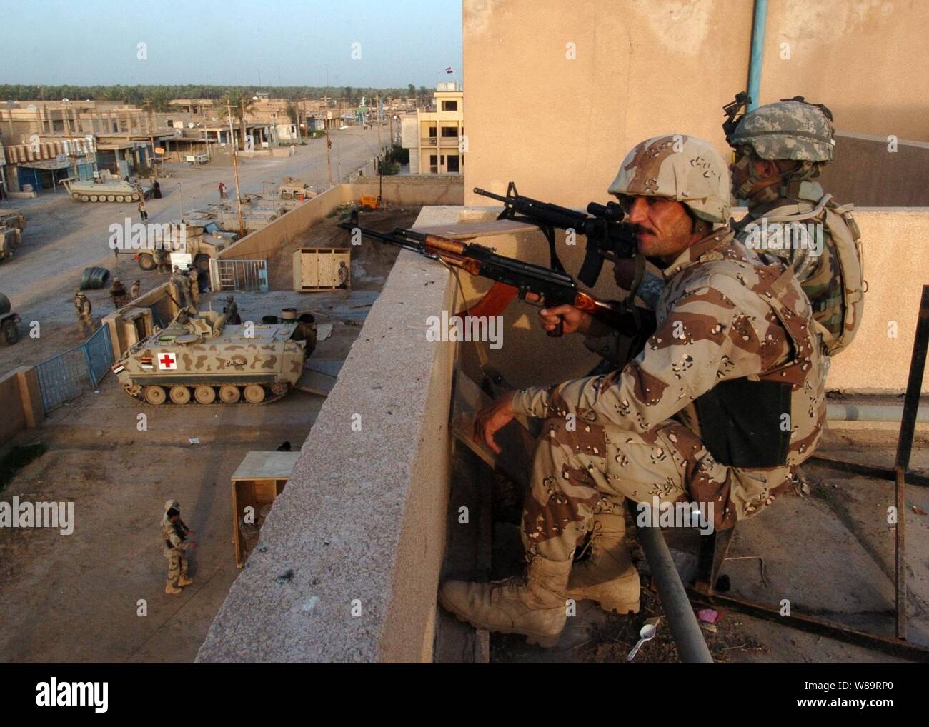 Iraqi army soldier Zatar Jeba (left) and U.S. Army Pfc. Yasuo Albert share a rooftop gun position on a coalition forces building during counter-insurgency operations in Tarmiya, Iraq, on March 25, 2006. Stock Photo