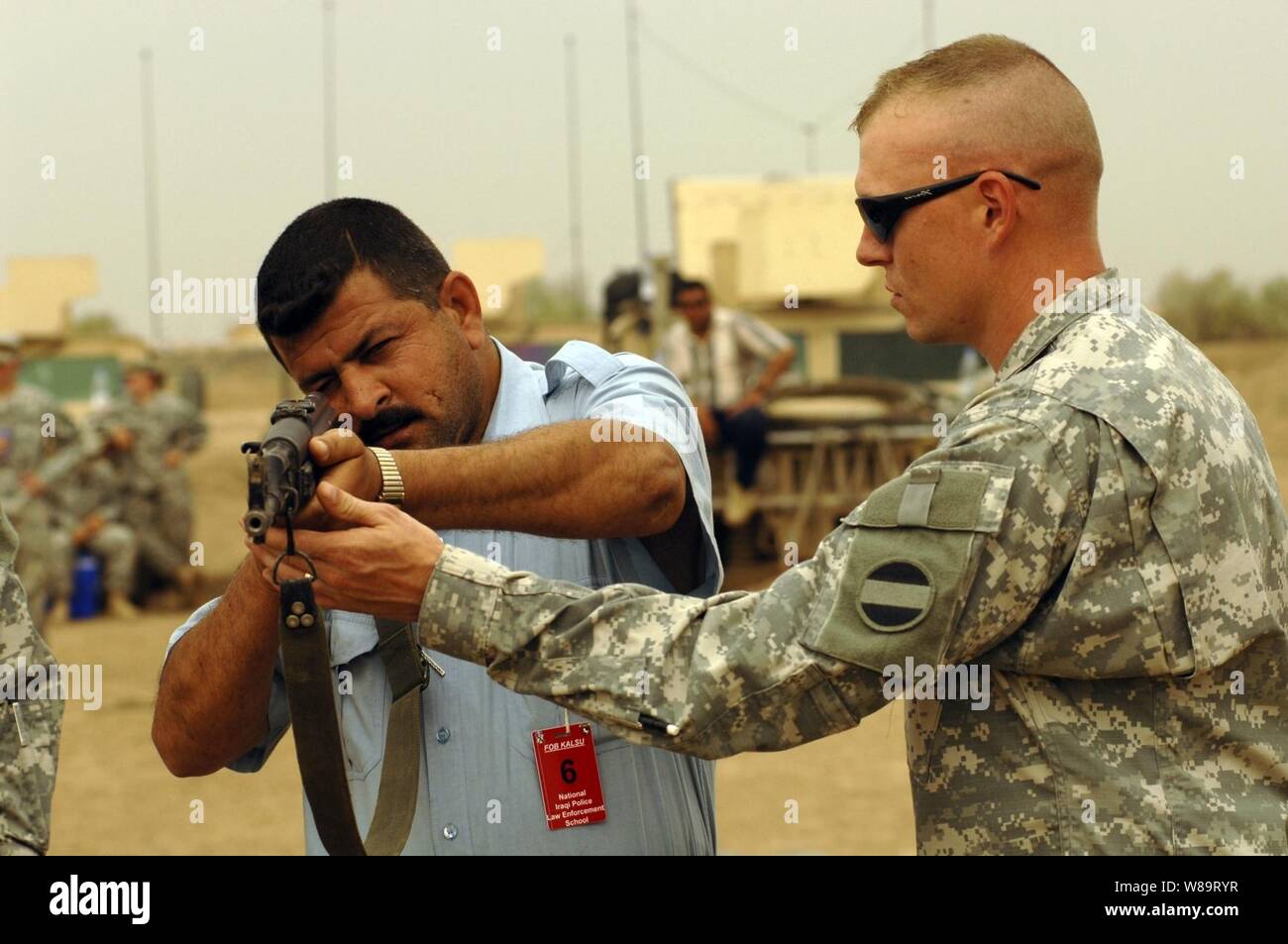 A soldier from the U.S. Armyís 988th Military Police Company trains an Iraqi police officer on how to properly hold a weapon during a two-week basic military training course at Forward Operating Base Kalsu, Iraq, on May 2, 2006. Stock Photo