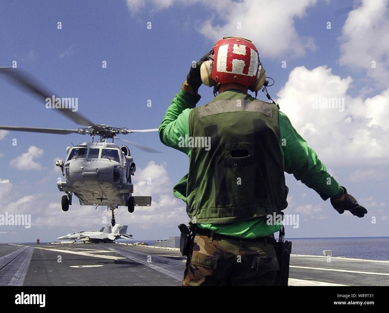 A U.S. Navy sailor guides an MH-60 Knighthawk onto the flight deck of the aircraft carrier USS Abraham Lincoln (CVN 72) during a vertical replenishment operation with the ammunition ship USNS Kiska (T-AE 35) on May 10, 2006.  The Lincoln and embarked Carrier Air Wing 2 are operating in the South China Sea. The Knighthawk is assigned to Helicopter Sea Combat Squadron 25. Stock Photo