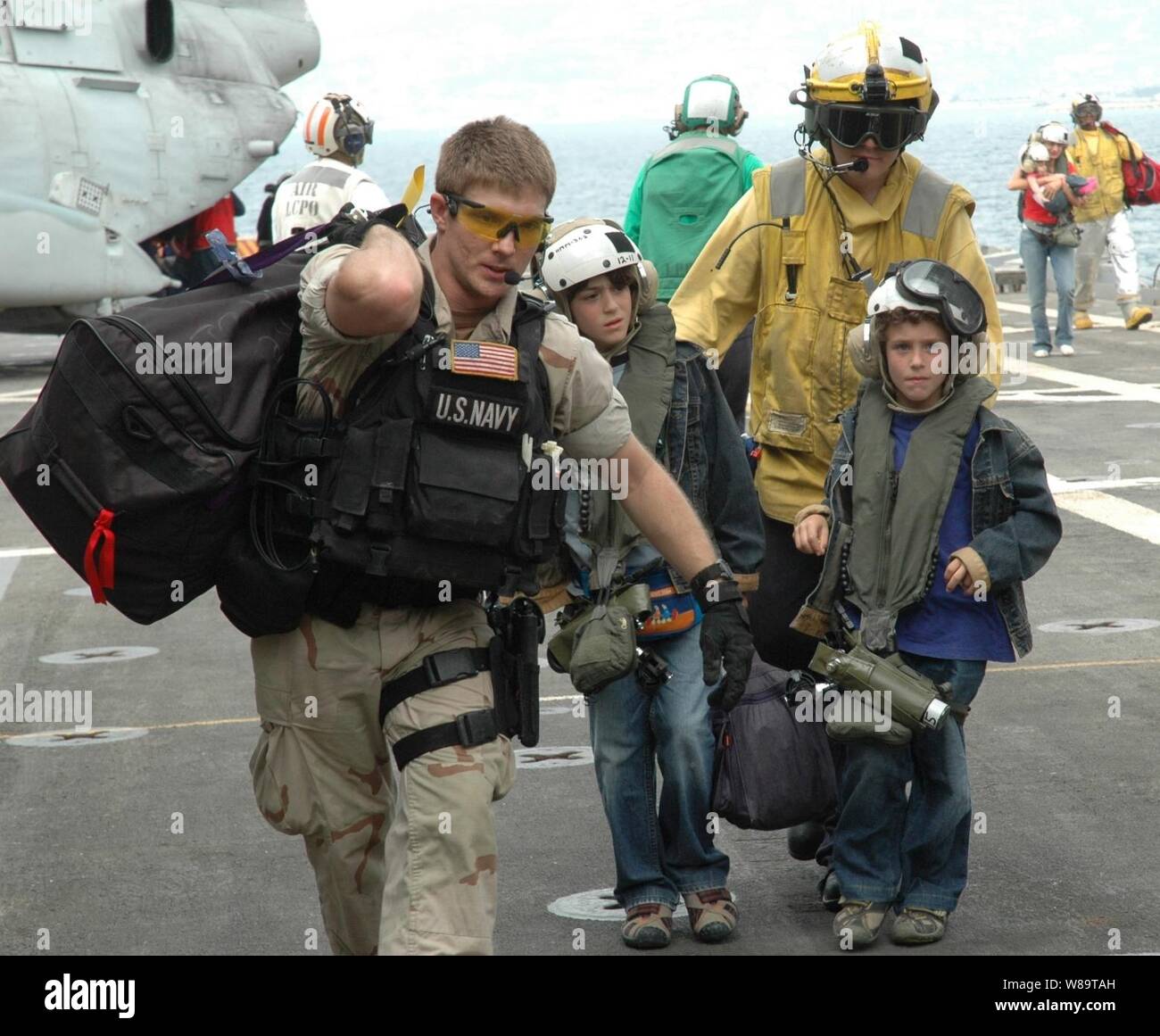U.S. Navy sailors assist two young American citizens as they arrive on the flight deck of the USS Trenton (LPD 14) as the ship operates off the coast of Lebanon on July 21, 2006.  At the request of the U.S. Ambassador to Lebanon and at the direction of the Secretary of Defense, the United States Central Command and elements of Task Force 59 are assisting with the departure of U.S. citizens from Lebanon.  The Trenton is an amphibious transport which is used to carry and land Marines, their equipment and supplies by embarked air cushion or conventional landing craft, amphibious vehicles, helicop Stock Photo