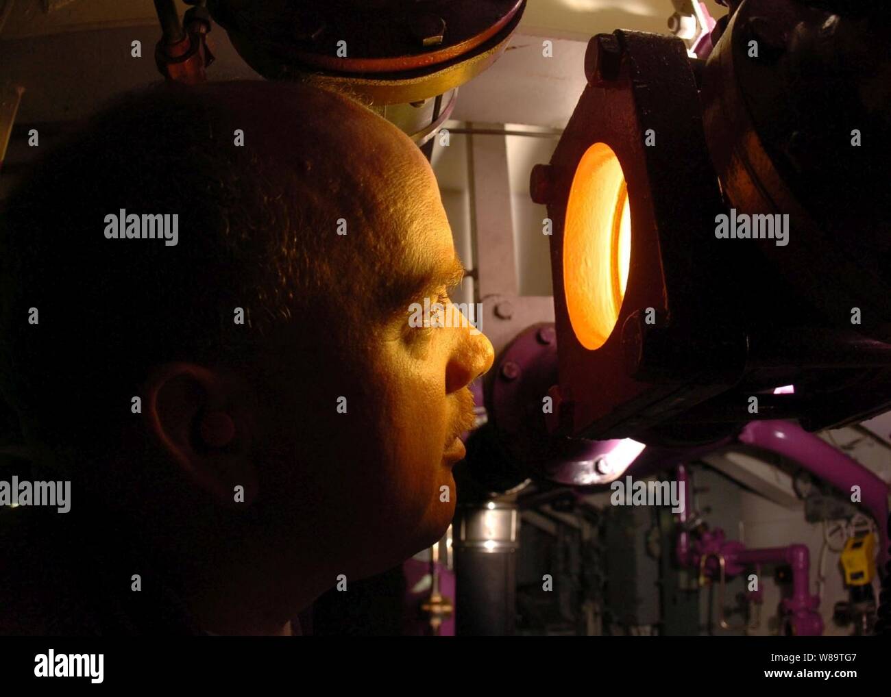 Navy Petty 3rd Class Kevin Luby looks through an illuminated sight glass to check for impurities in aviation fuel inside the JP-5 pump room aboard the aircraft carrier USS John C. Stennis (CVN 74) on Oct. 11, 2006.  Luby is a Navy aviation boatswainís mate who specializes in aircraft fuel. Stock Photo