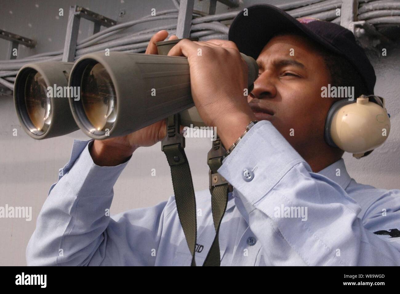U.S. Navy Petty Officer 2nd Class Christopher Reid uses binoculars to look at commercial ships near the aircraft carrier USS Kitty Hawk's (CV 63) as the ship operates in the Pacific Ocean on March 3, 2008.  Reid is a Navy Intelligence Specialist onboard the carrier. Stock Photo