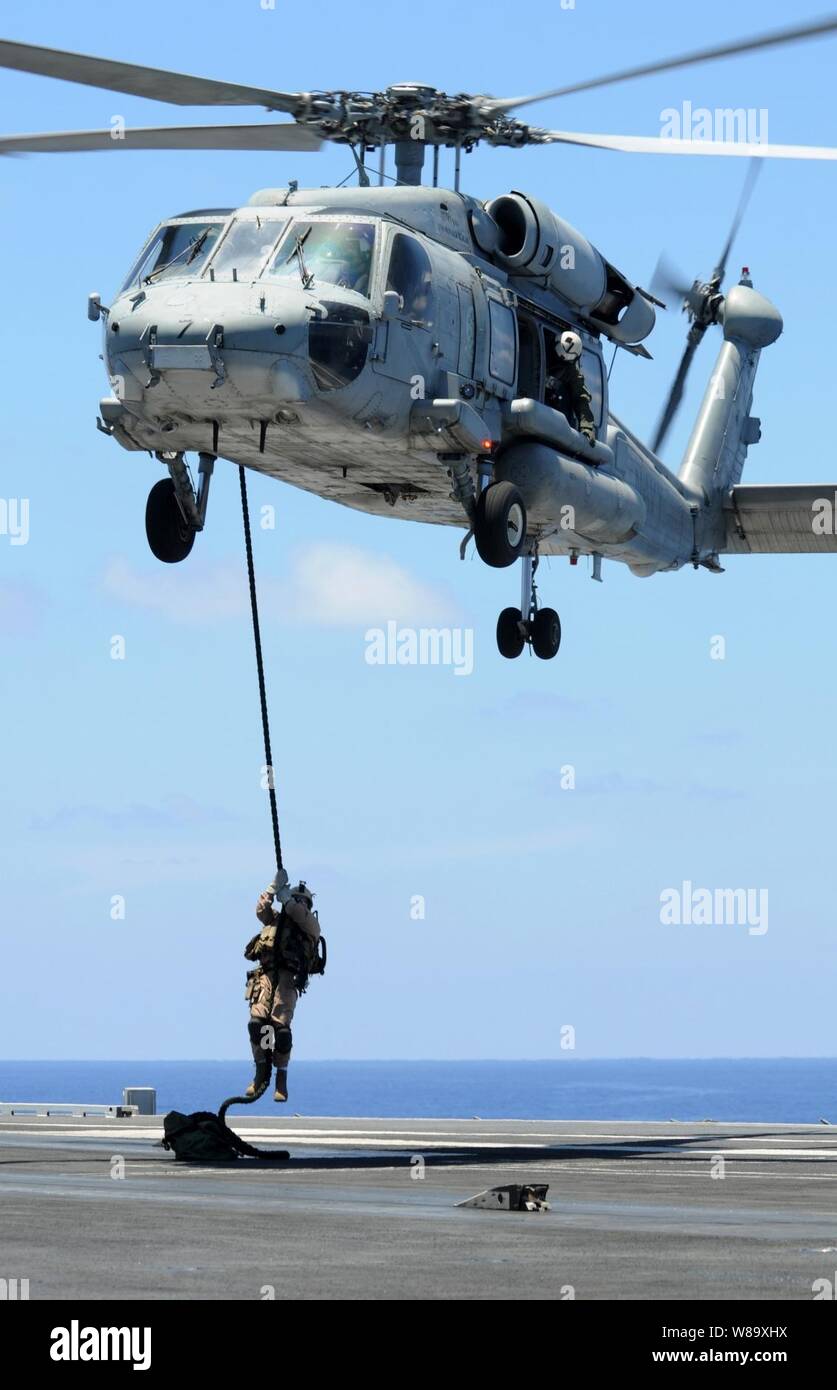 A U.S. Navy explosive ordnance disposal technician assigned to Mobile Unit 11, Platoon 0-2, fast-ropes onto the flight deck of the aircraft carrier USS Ronald Reagan (CVN 76) during a training exercise in the Pacific Ocean on June 12, 2009.  The exercise is a combined effort between the explosive ordnance disposal team and Helicopter Anti-submarine Squadron 4.  The Reagan is underway on deployment to the western Pacific. Stock Photo