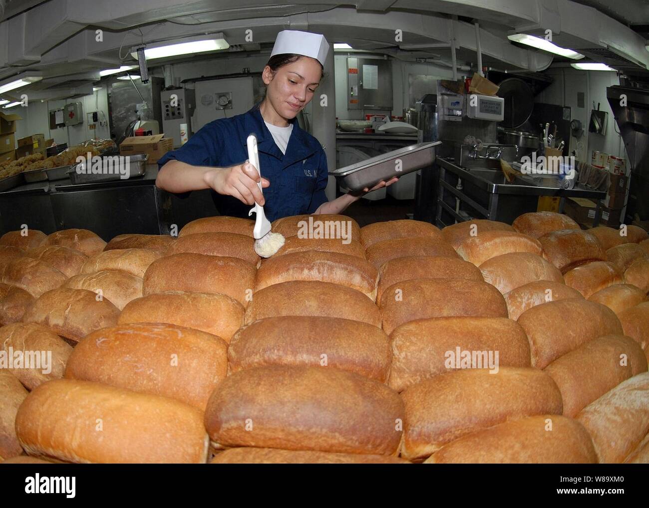 U.S. Navy Seaman Samantha Garza butters loaves of freshly baked bread in the bakeshop aboard the aircraft carrier USS George Washington (CVN 73) in the Pacific Ocean on July 16, 2009.  The George Washington is participating in Talisman Sabre 2009, a biennial joint military exercise between the U.S. and Australia. Stock Photo