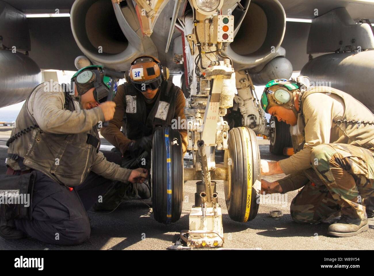 U.S. Navy sailors assigned to Strike Fighter Squadron 97 change the tires on the nose landing gear of an F/A-18C Hornet aircraft aboard the aircraft carrier USS Nimitz (CVN 68) underway in the Indian Ocean on Jan. 28, 2010.  The Nimitz Carrier Strike Group is conducting operations in the U.S. 7th Fleet area of responsibility in support of maritime security. Stock Photo