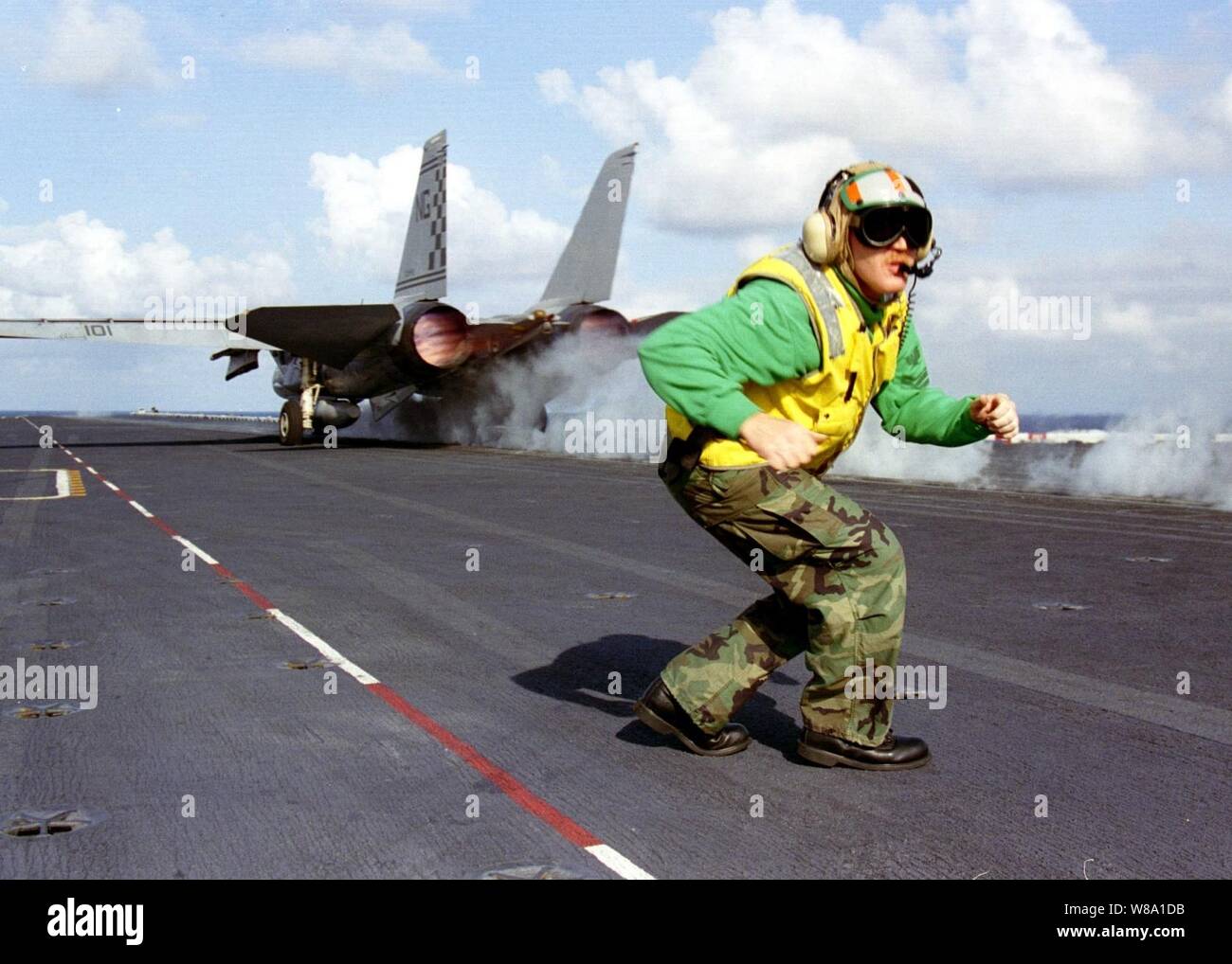 As a F-14 Tomcat roars down one of the four steam driven catapults of the aircraft carrier USS Nimitz (CVN 68) Petty Officer 1st Class John Macaby moves quickly to ready the next aircraft for launch during flight operations in the Persian Gulf on Nov. 4, 1997.  The Nimitz and embarked Carrier Air Wing 9 are operating in the Persian Gulf in support of the U.S. and coalition enforcement of the no-fly-zone over Southern Iraq. Macaby, from Kent, Wash., is a Navy aviation boatswainХs mate (equipment). Stock Photo