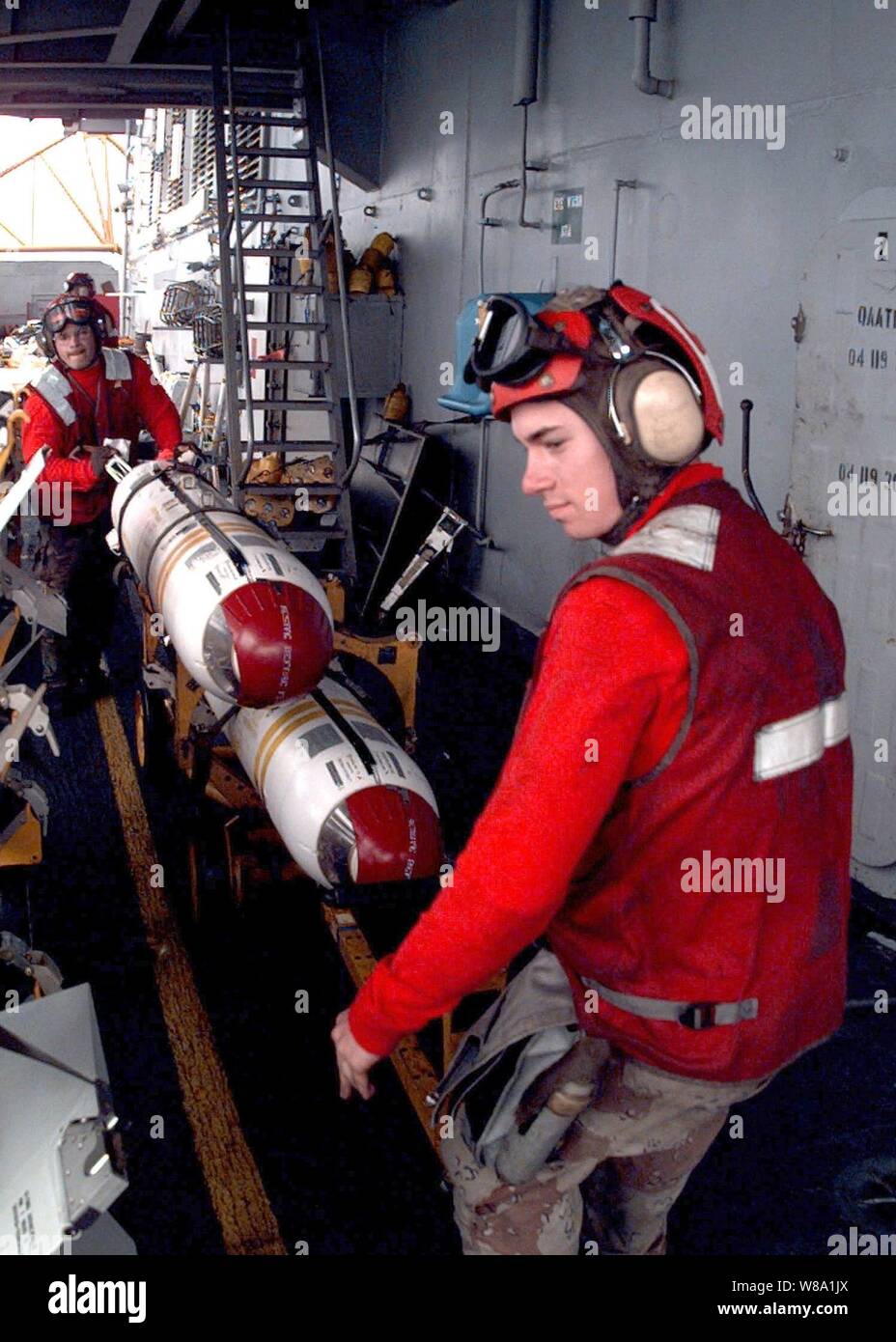 Airman David Rodriguez (right) guides a cart of cluster bombs into the staging area for munitions on the flight deck of the USS Independence (CV 62) while the ship operates in the Persian Gulf on Feb. 11, 1998.  Independence and its embarked Carrier Air Wing 5 are on station in the Persian Gulf in support of Operation Southern Watch which is the U.S. and coalition enforcement of the no-fly-zone over Southern Iraq.  Rodriguez is a Navy aviation ordnanceman. Stock Photo
