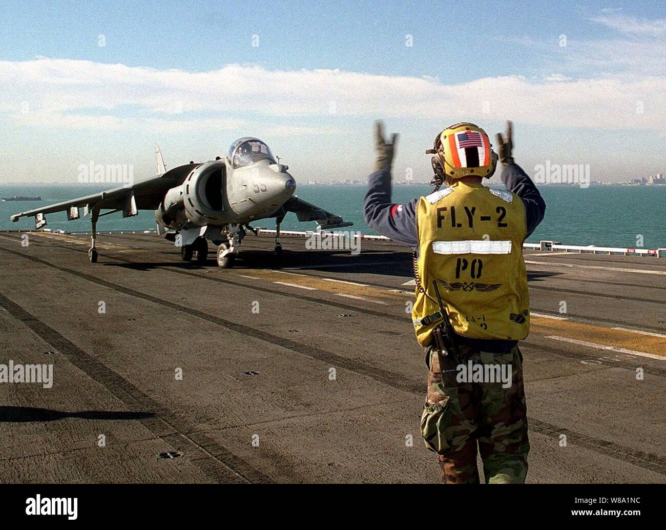 Petty Officer 2nd Class Mark Agurrie signals the pilot of an AV-8B Harrier to taxi aboard the amphibious assault ship USS Tarawa (LHA 1) as the ship operates off the coast of Kuwait City on March 23, 1998.  Tarawa is deployed to the Persian Gulf in support of Operation Southern Watch, which is the U.S. and coalition enforcement of the no-fly-zone over Southern Iraq.  Agurrie is a Navy aviation boatswain's mate. Stock Photo