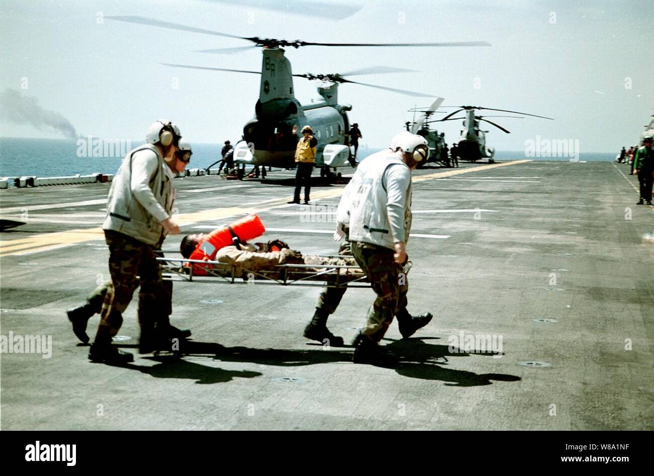 U.S. Marines from the Combat Cargo Platoon rush an injured sailor from the merchant vessel Seal-Land Mariner, seen ablaze in the background, to the medical department aboard the U.S. Navy amphibious assault ship USS Wasp (LHD 1) in the Mediterranean Sea on April 18, 1998.  Search and rescue crew members, helicopters and an 18-person fire-fighting team from the Wasp responded to an emergency distress call from the merchant vessel in the Mediterranean Sea, approximately 85 miles west of Crete.  A U.S. Navy CH-46 Sea Knight helicopter air-lifted two of the merchant vessel crew members to the Wasp Stock Photo
