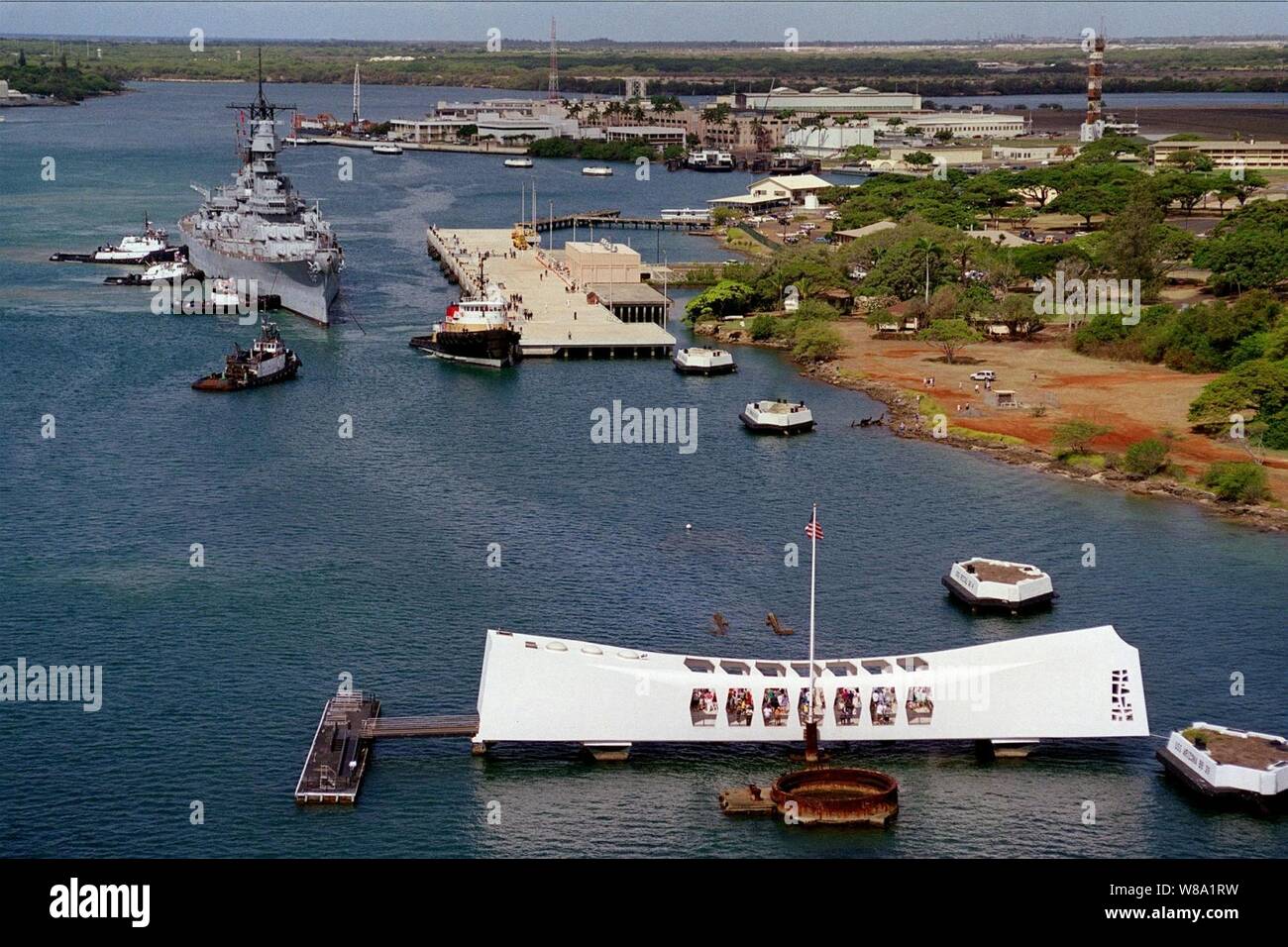 Tug boats push the battleship USS Missouri (BB 63) to its new berth at Ford Island, on June 22, 1998, as it joins the USS Arizona Memorial (foreground) in Pearl Harbor, Hawaii.  Secretary of the Navy John H. Dalton signed the Donation Agreement on May 4th, allowing Missouri to be used as a museum near the Arizona Memorial as symbols of the beginning and the end of World War II.  The Missouri was towed 2,600-miles across the Pacific Ocean from Bremerton, Wash. Stock Photo