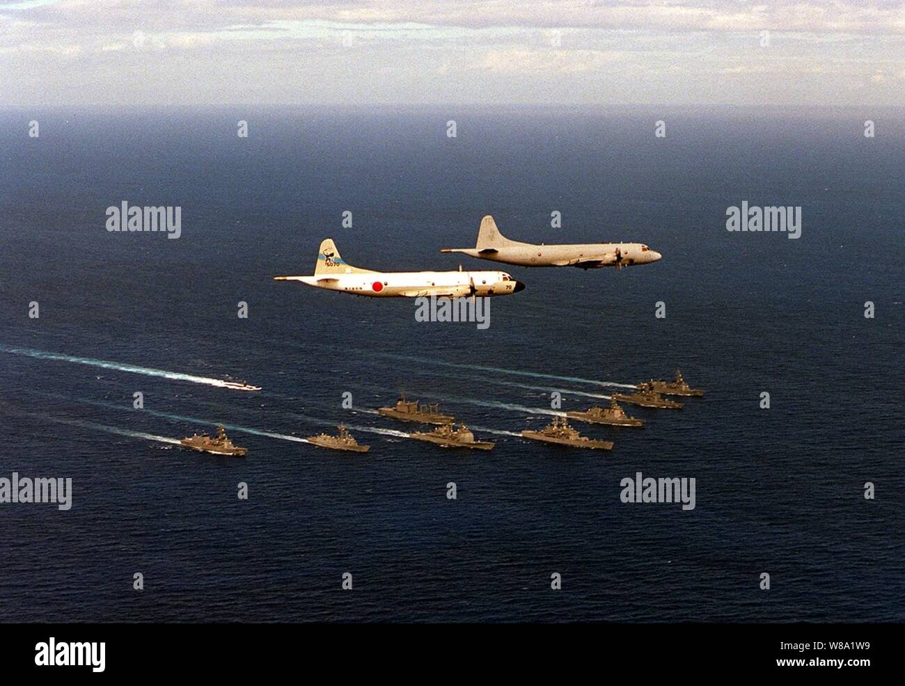 A U.S. Navy P-3 Orion from the Skinny Dragons of Patrol Squadron 4 leads a Japanese P-3 in flight over a Bilateral Force of U.S. and Japanese ships.  The ships in formation are; USS Key West(SSN 722), USS Vandergrift(FFG 48), USS California(CGN 36), USS Chancellorsville(CG 62),USS Port Royal(CG 73), JDS Kirishima(DDG 174), JDS Shirane(DDH 143), JDS Murasame(DD101), JDS Harusame(DD 102), and JDS Towada(AOE 422).  The operations are part of RIMPAC 98. Stock Photo