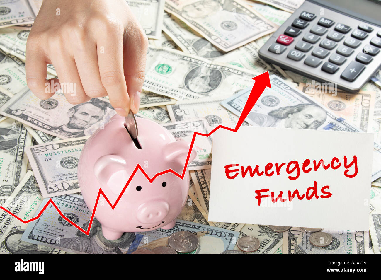 United States bank notes and coins with a calcultor, piggy bank, and hand placing coin into piggy bank and a card that says Emergency Funds Stock Photo
