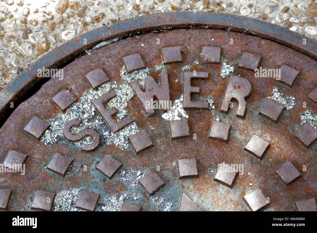 A rusty manhole cover with sewer displayed on it. Stock Photo