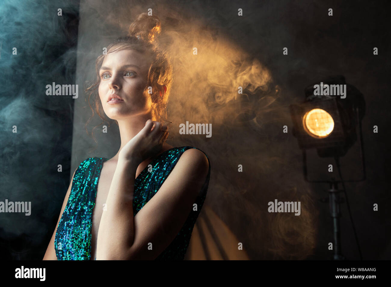 Charning woman in spotlight beam and smoke looking into the distance Stock Photo