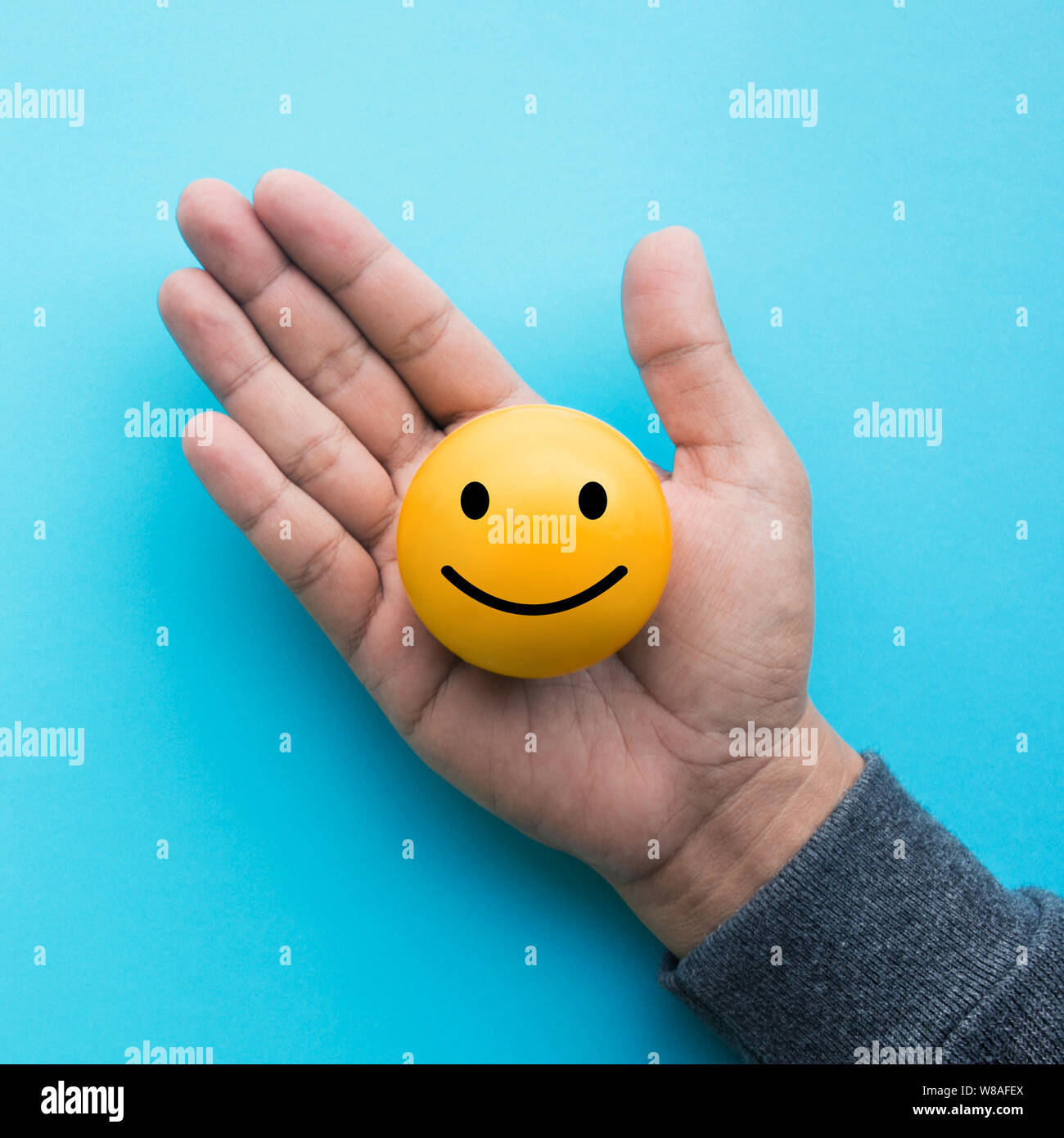 Mele hand holding yellow  emoticon ball on blue color background Stock Photo
