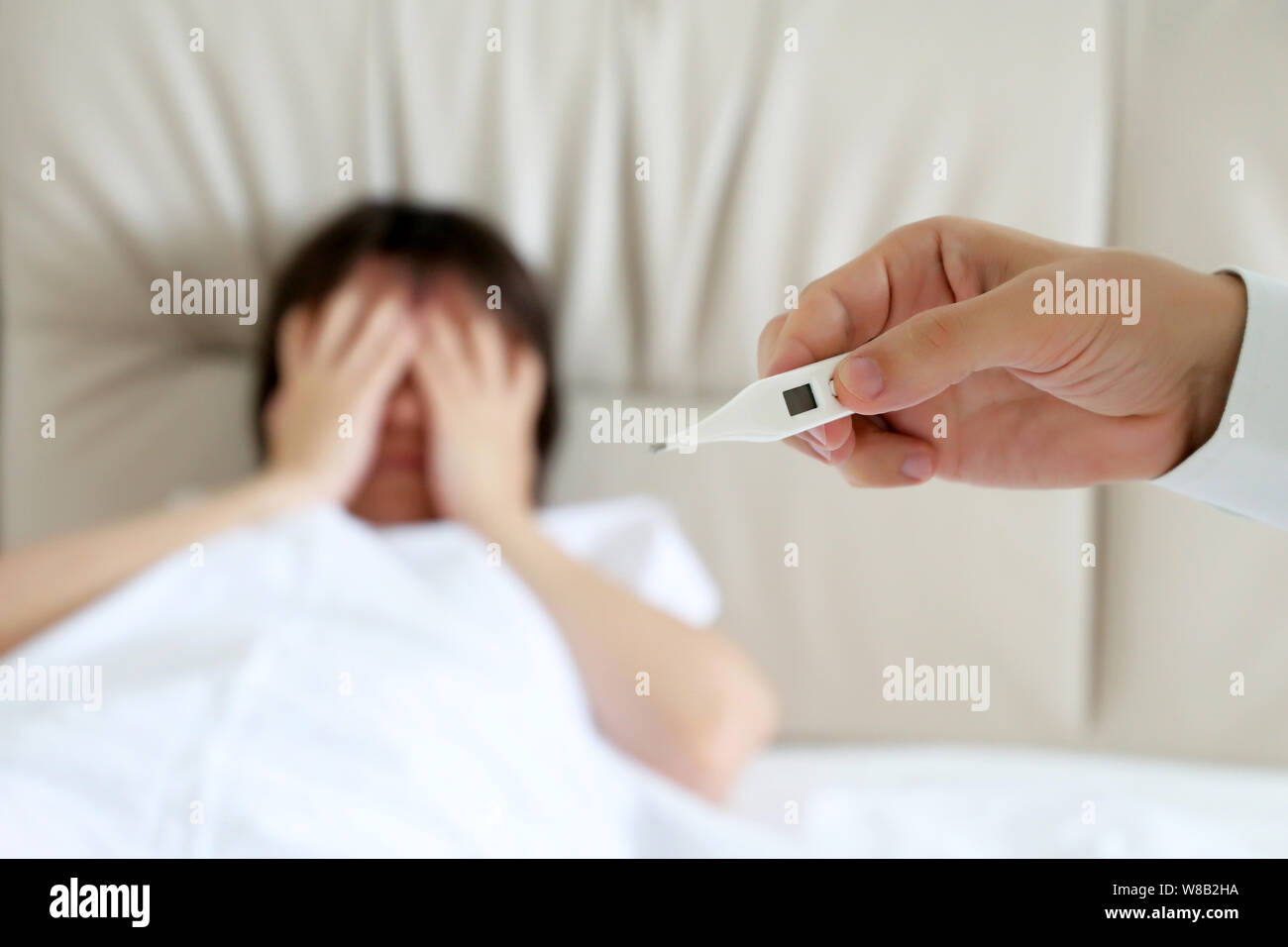 Sick woman lying in a bed, digital thermometer in male hand. Doctor measuring body temperature of patient, concept of cold and flu, fever, illness Stock Photo