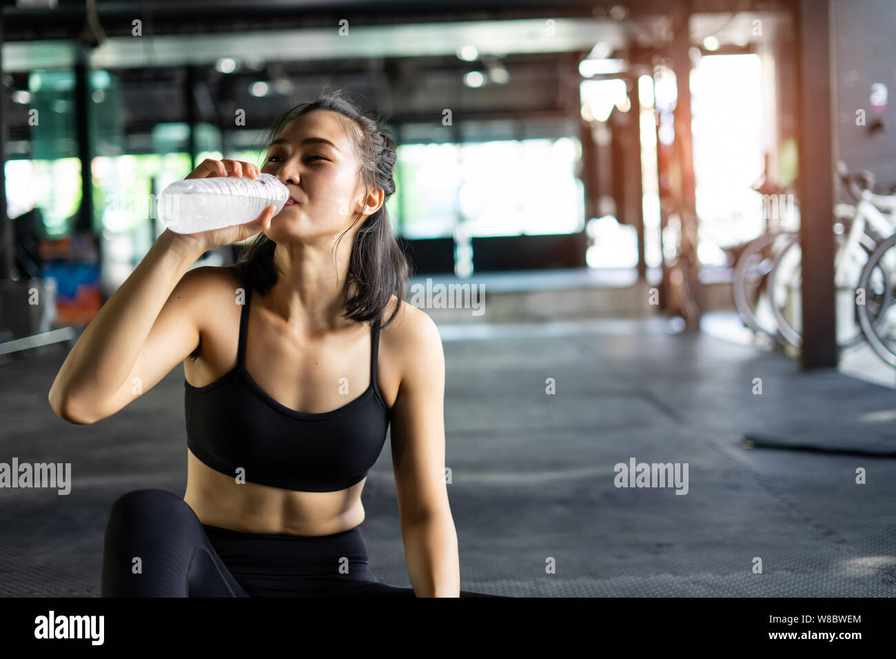 Sporty beautiful woman exercising relax and drink water with training equipment blurry background, Healthy life and gym exercise equipments and sports Stock Photo