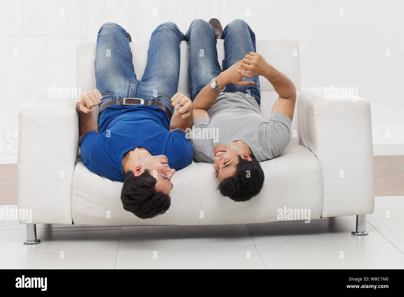 Two friends lying upside down on sofa Stock Photo