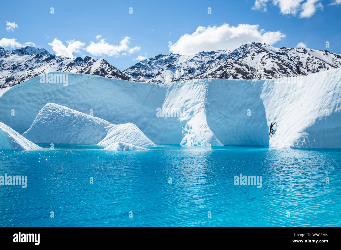 Massive blue lake on the Matanuska Glacier with an ice climber ascending up from just above the blue water. Stock Photo