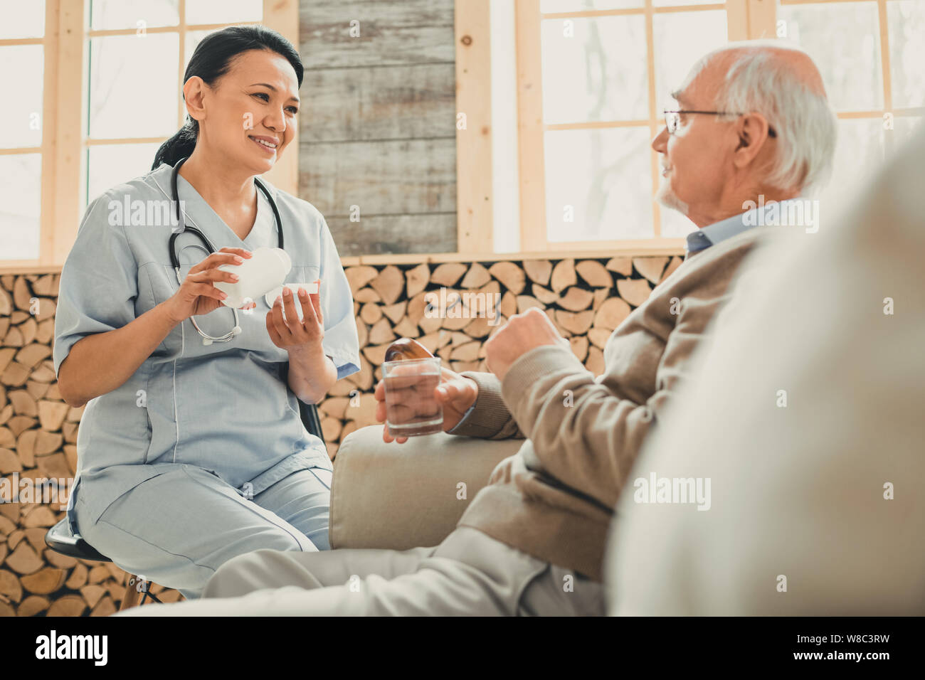 Smiling kind woman sitting in chair against old man Stock Photo