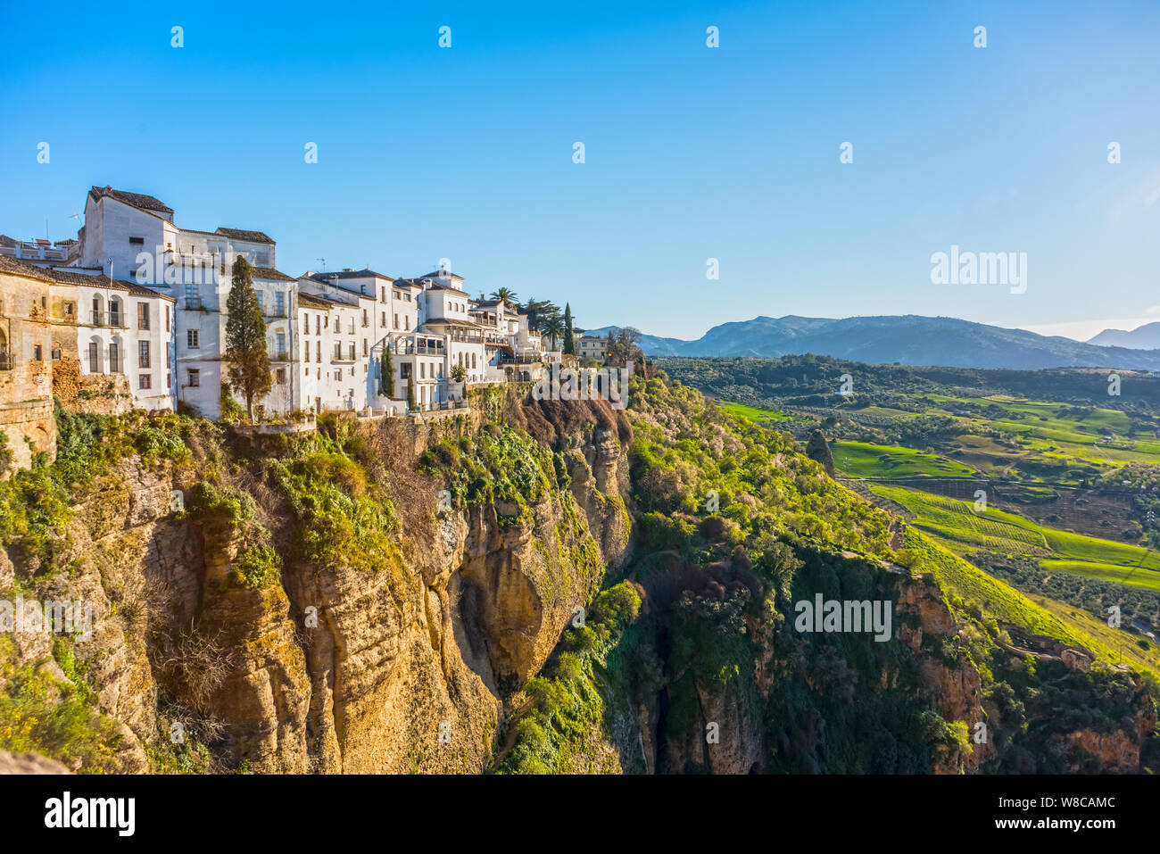 Ronda, Spain: Landscape of white houses on the green edges of steep cliffs with mountains in the background. Stock Photo