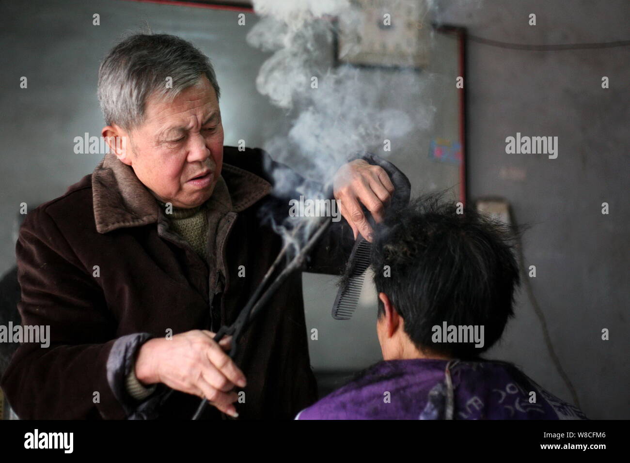 Chinese Barber Wang Weimei Left Uses A Pair Of Hot Fire Tongs To Perm The Hair Of A Customer At His Shop In Jinshi Town Santai County Mianyang Cit Stock Photo
