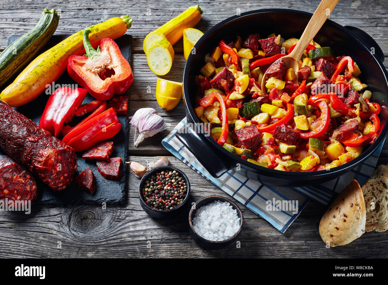 Pisto manchego - vegetable stew with chorizo sausages in a black pan on a rustic wooden table, spanish cuisine, horizontal view from above, Stock Photo
