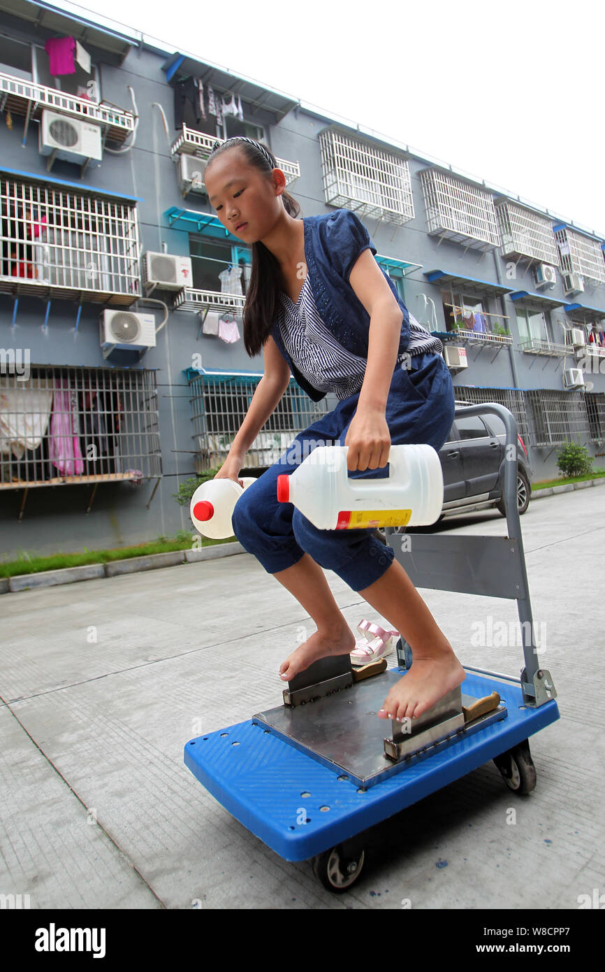 A 13-year-old girl surnamed Xie carries bottles of water, weighing 5 kilograms, while standing barefooted on the blades of meat cleavers in Wenzhou ci Stock Photo