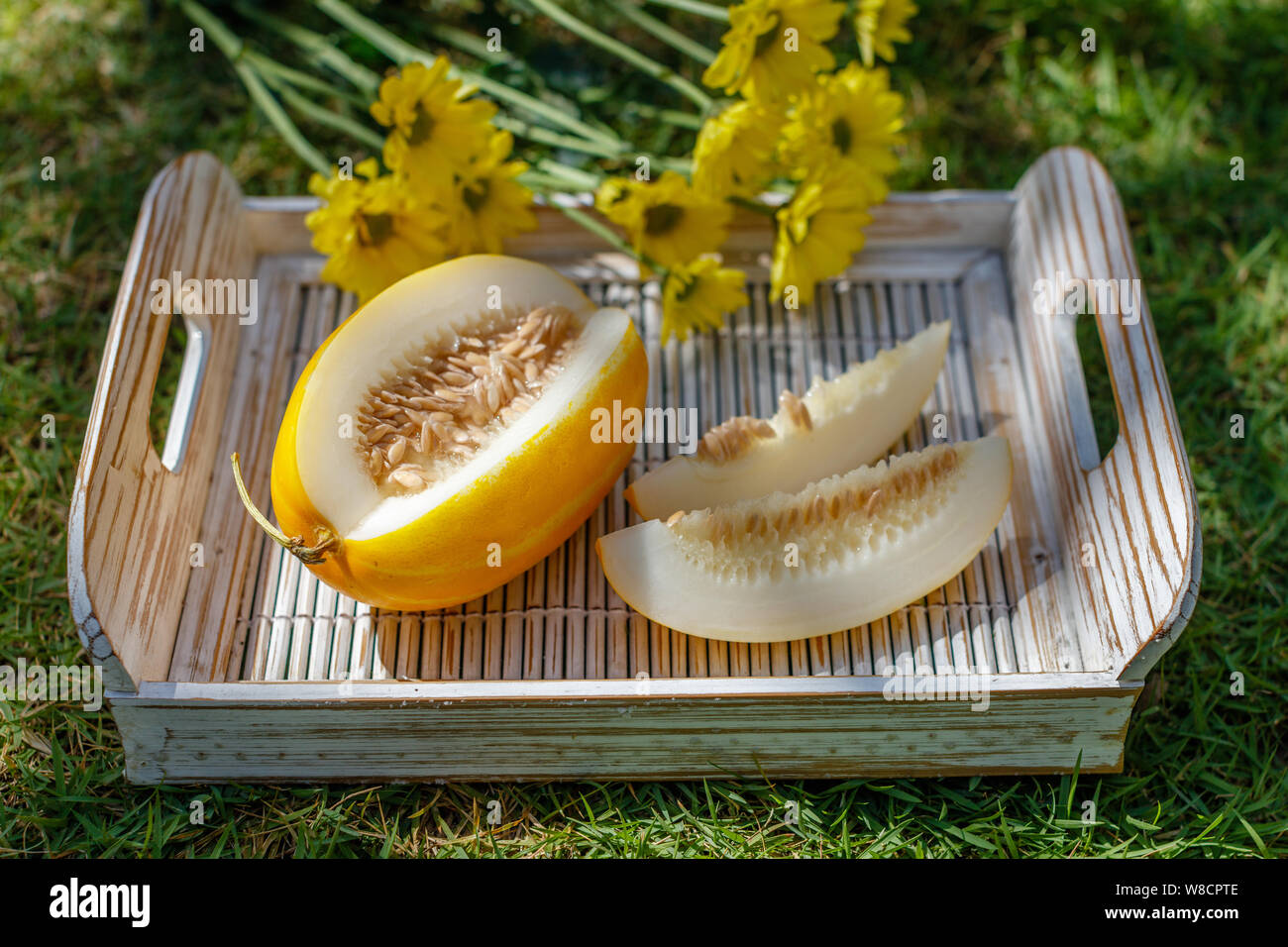 Cut Yellow Oriental melon (Korean melon)  on a white wooden tray. Yellow Chrysanthemum on the background. Stock Photo