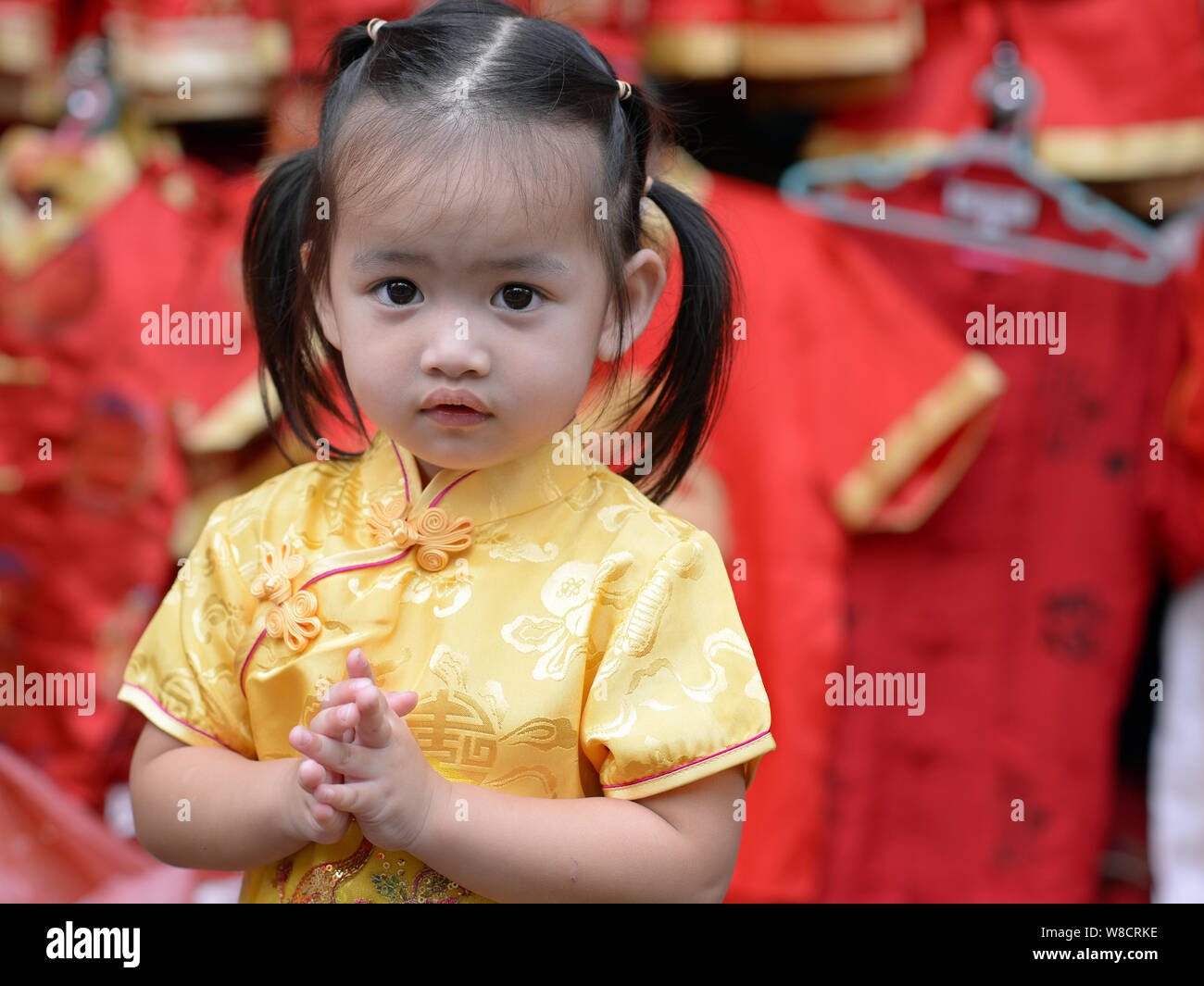 Cute little Thai girl wears a yellow Chinese dress (cheongsam) during Chinese New Year and greets with the traditional wai gesture. Stock Photo
