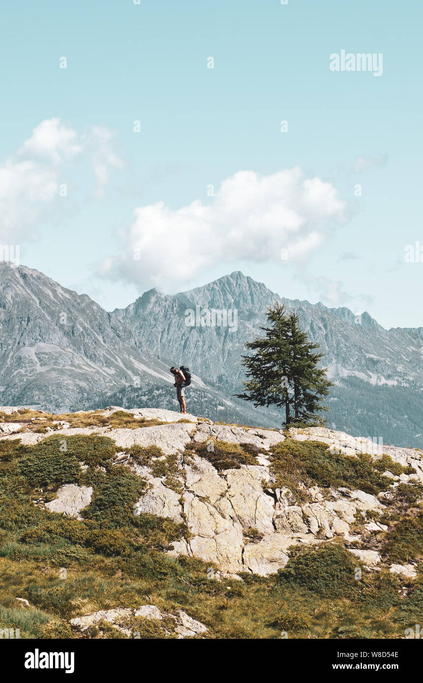 Vertical picture of adventurous man hiking in the mountains. Standing on the edge of a rock. Backpacking traveler. Adventure concept. Active lifestyle Stock Photo