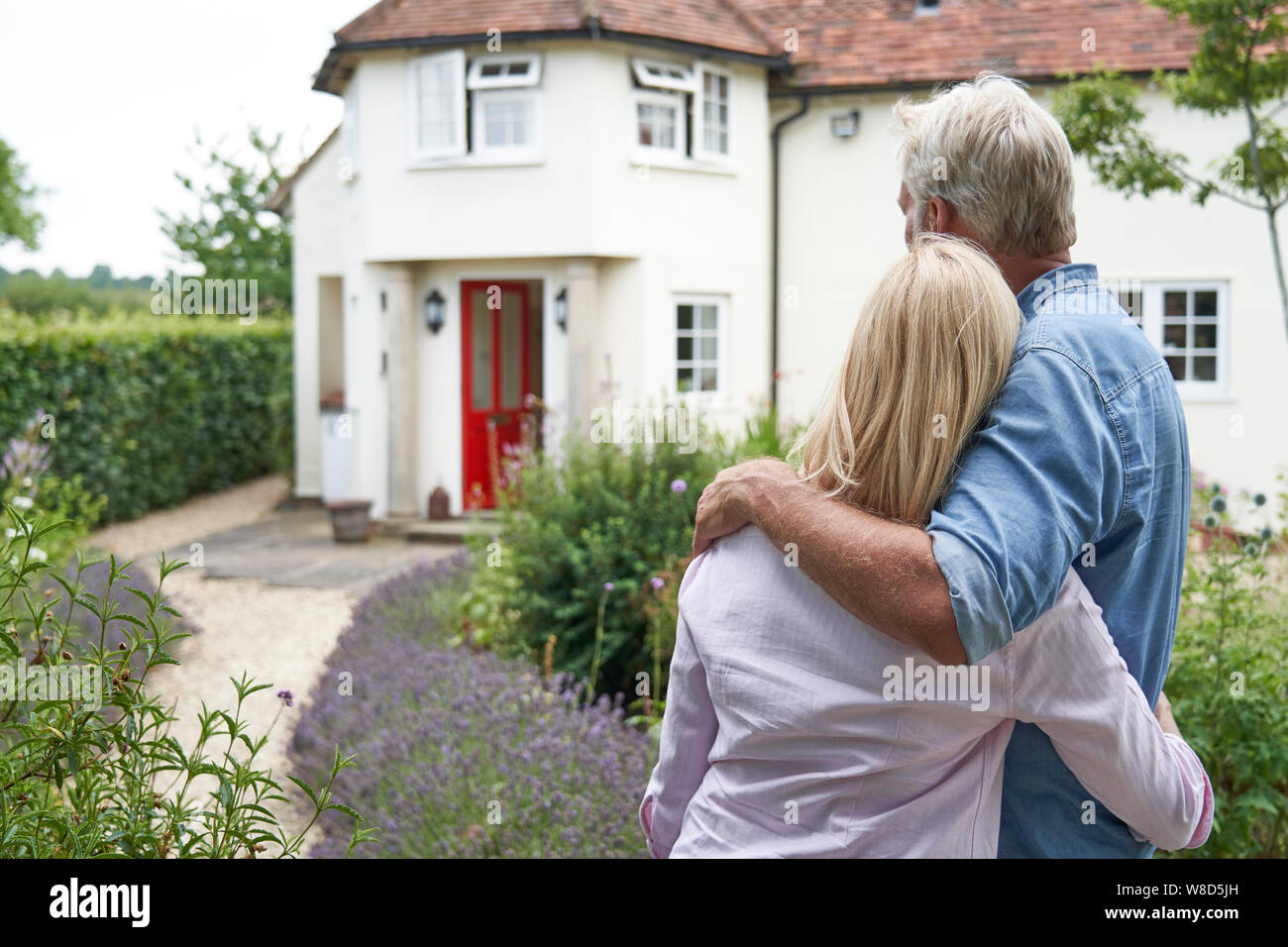 Rear View Of Mature Couple Standing In Garden Look At Dream Home In Countryside Stock Photo