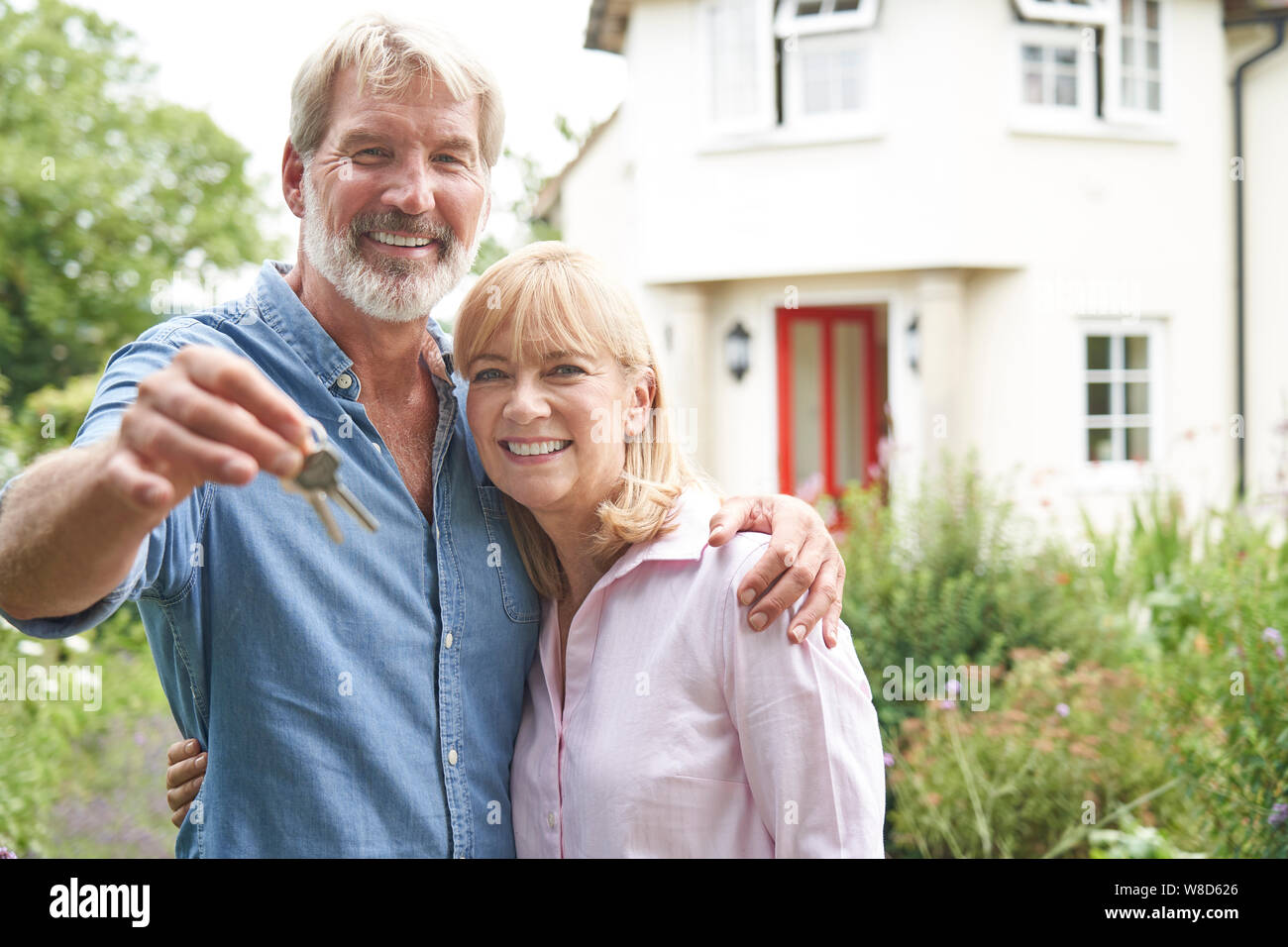 Portrait Of Mature Couple Standing In Garden In Front Of Dream Home In Countryside Holding Keys Stock Photo