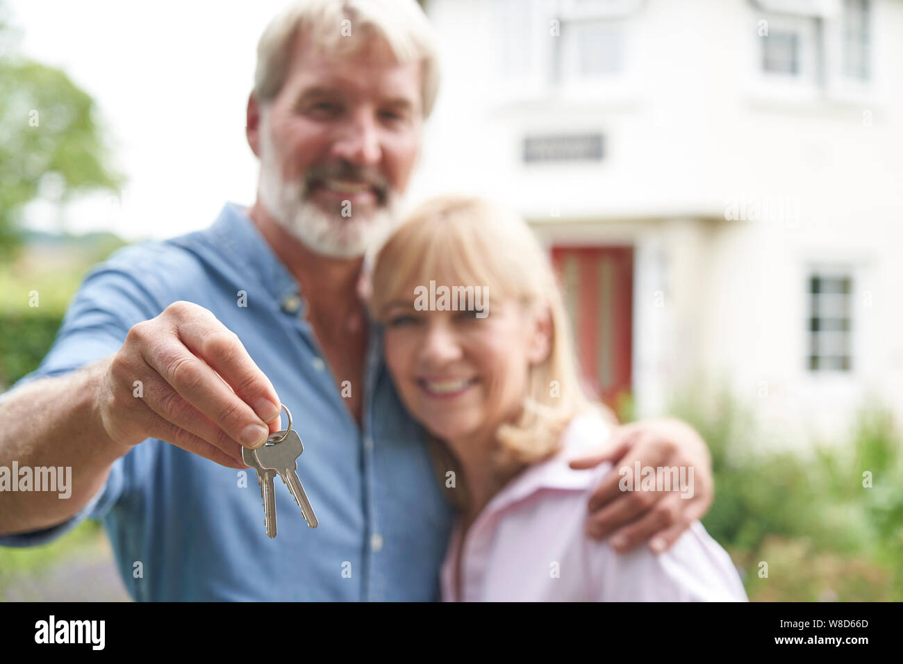 Portrait Of Mature Couple Standing In Garden In Front Of Dream Home In Countryside Holding Keys Stock Photo