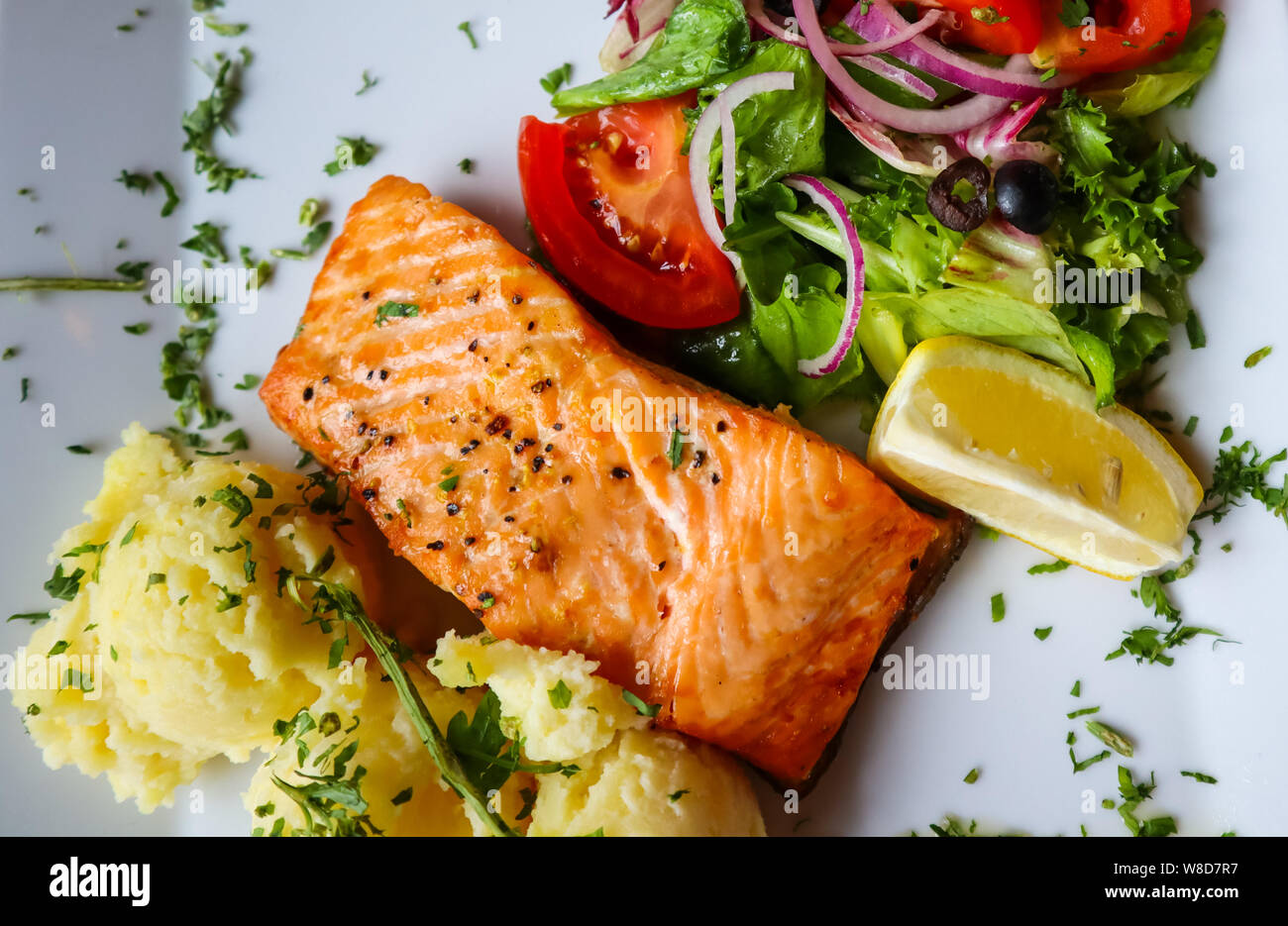 Baked salmon with mash potato, lemon, tomatoes, red onions, olives and