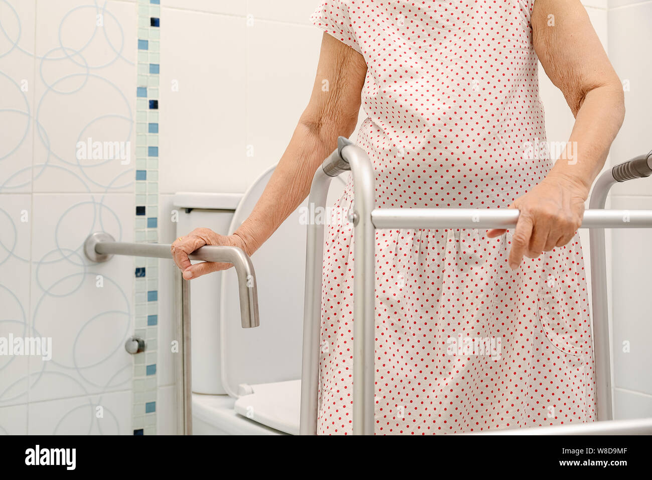 Elderly woman holding on handrail in toilet. Stock Photo