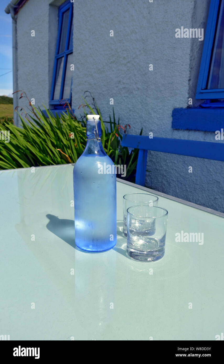 Bottle of cold tap water and two glasses on a garden table in summer Stock Photo
