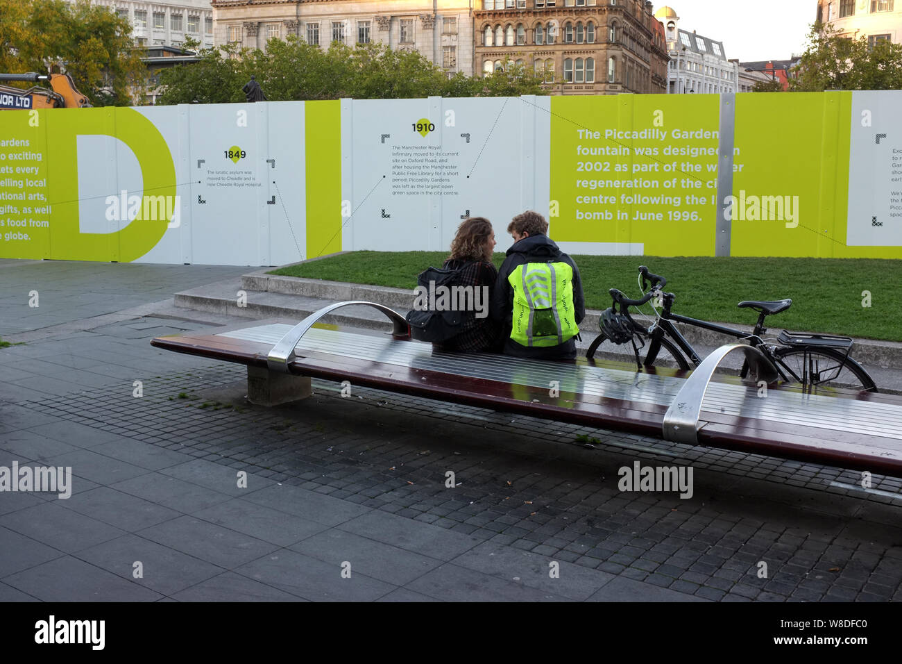 Young couple talking on a bench in front of hoarding during a revamp / modernisation of Piccadilly Gardens Manchester, England UK. photo DON TONGE Stock Photo