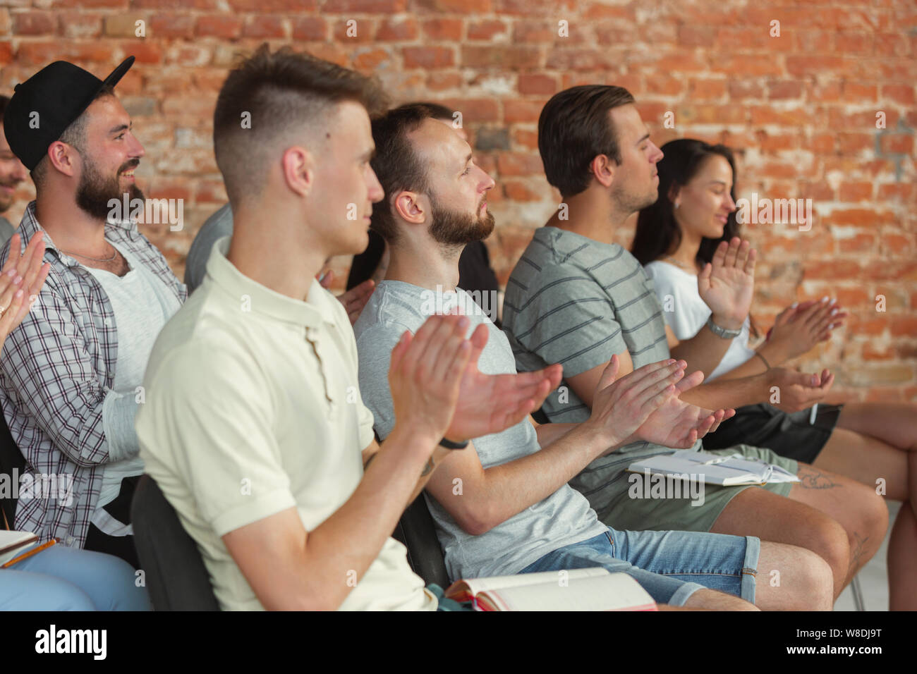 Group of students listen to presentation at university workshop. Audience or conference hall. Greeting the speaker before the lecture starts. Scientific conference event, training. Education concept. Stock Photo