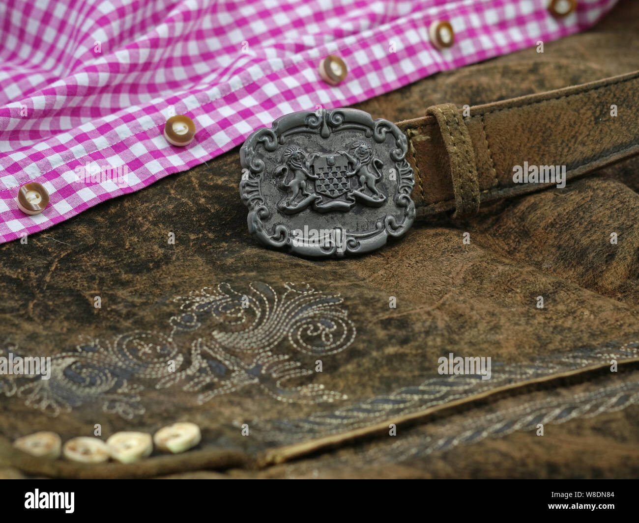 close up bavarian lether belt with coat of arms on lederhose and pink check shirt, traditional clothing for Oktoberfest Stock Photo
