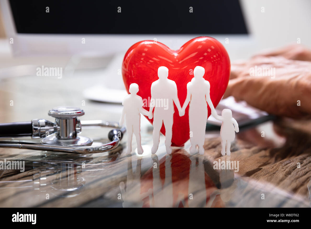 Red Heart With Family In Front Of Doctor Working On Computer Stock Photo