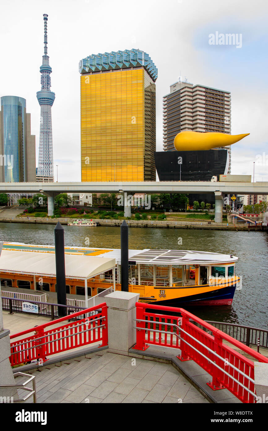 Asahi Beer Hall is part of the Asahi Breweries headquarters on the east bank of the Sumida River, Tokyo, Japan. Also shows water bus and Skytree tower Stock Photo