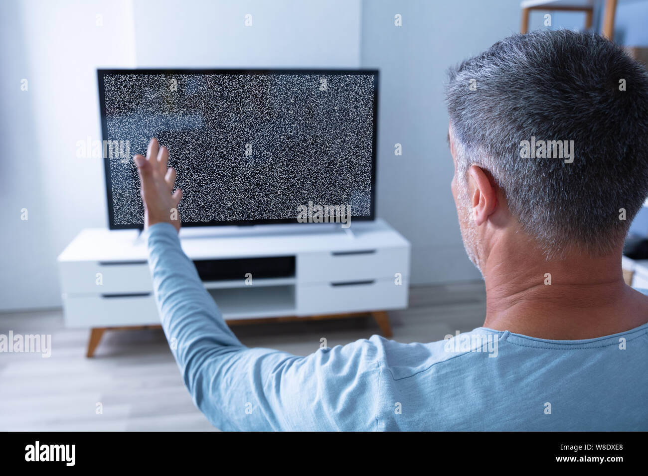 Man Sitting On Sofa In Front Of Television With No Signal Stock Photo