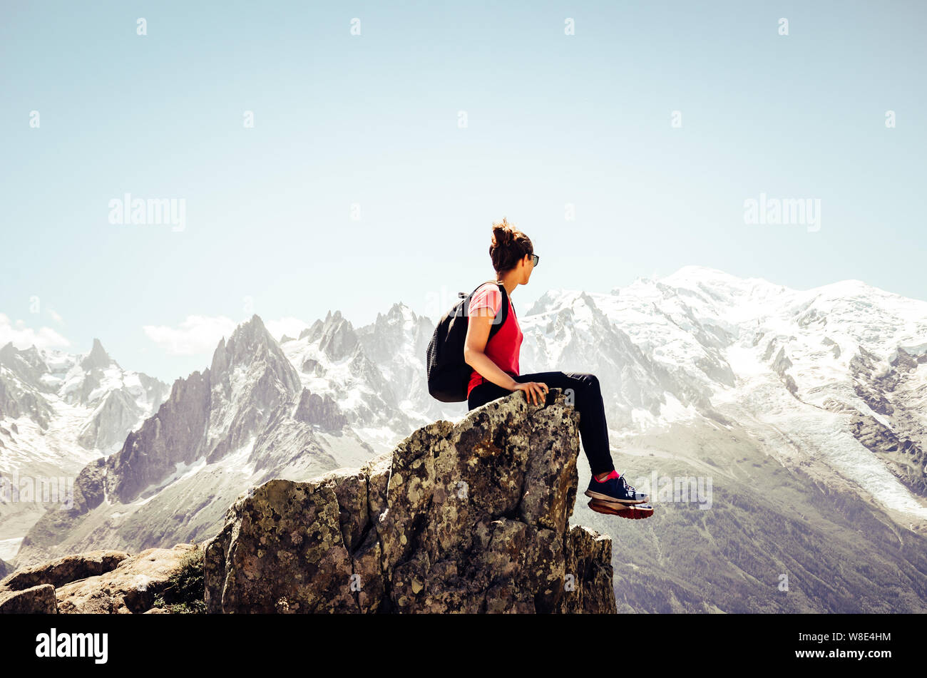 Young female traveller sitting on the edge of rocks. High mountains in background. Woman backpacking. Hiking adventure. Active lifestyle. Explore conc Stock Photo