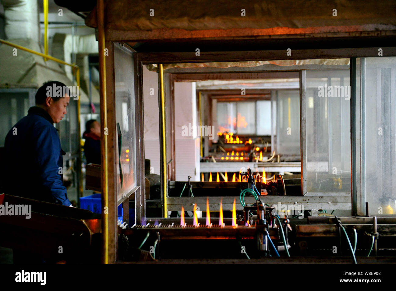Chinese workers monitor mercury-in-glass thermometers being heated in flames to have the necks of the glass tubes narrowed at the plant of Jiangsu Yuy Stock Photo