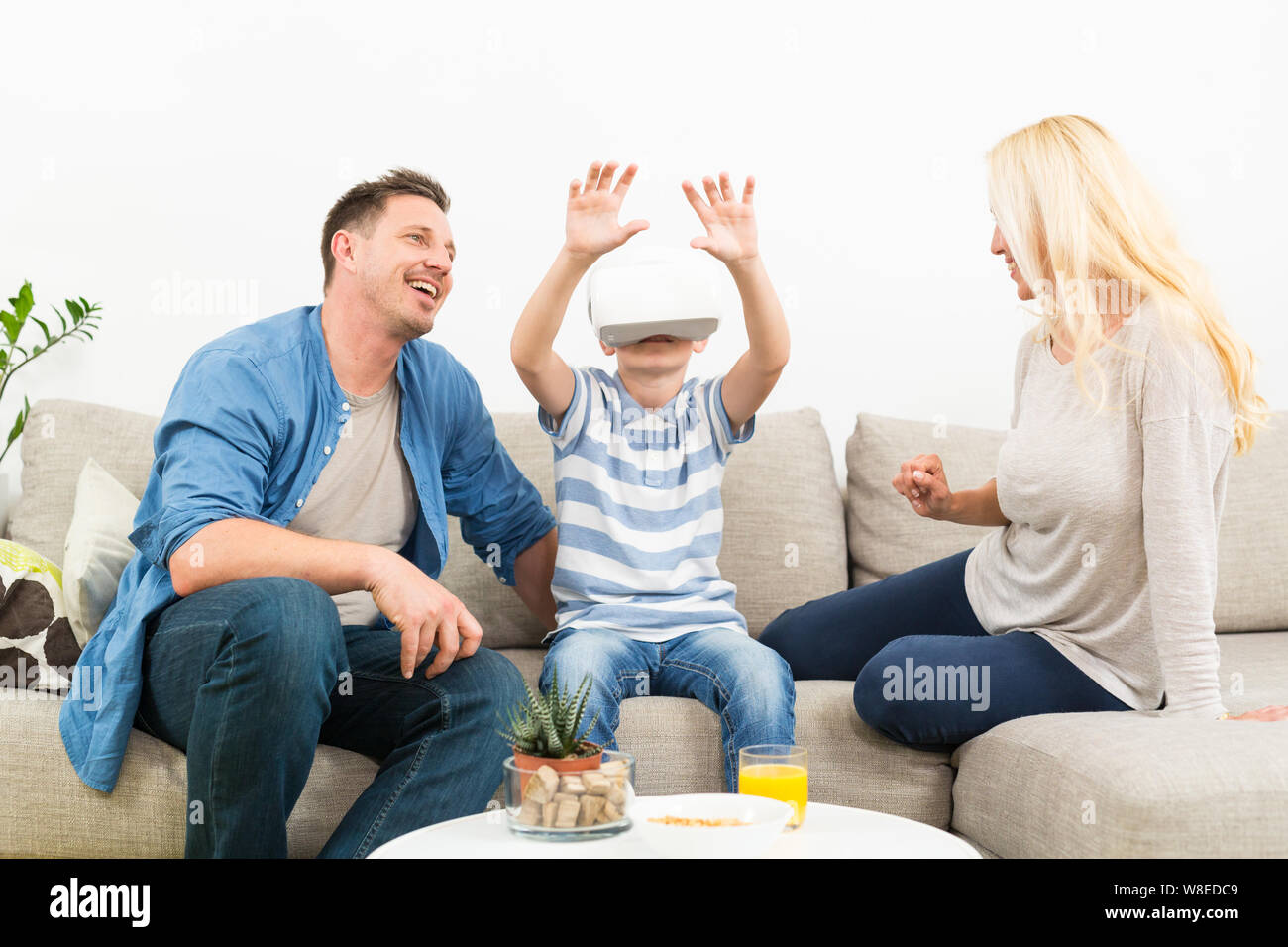 Happy family at home on living room sofa having fun playing games using virtual reality headset Stock Photo