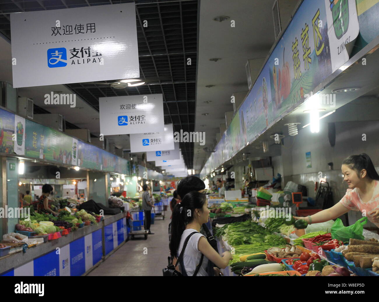 Chinese customers shop for vegetables under advertisements for mobile payment service Alipay of Alibaba Group at a free market in Wenzhou city, east C Stock Photo